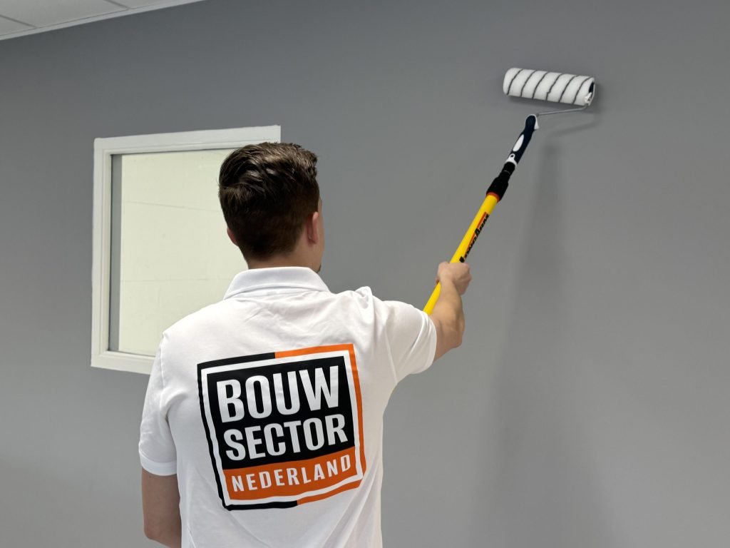 Schilder met het Bouwsector Nederland-logo op zijn rug rolt een grijze muur naast een binnenraam