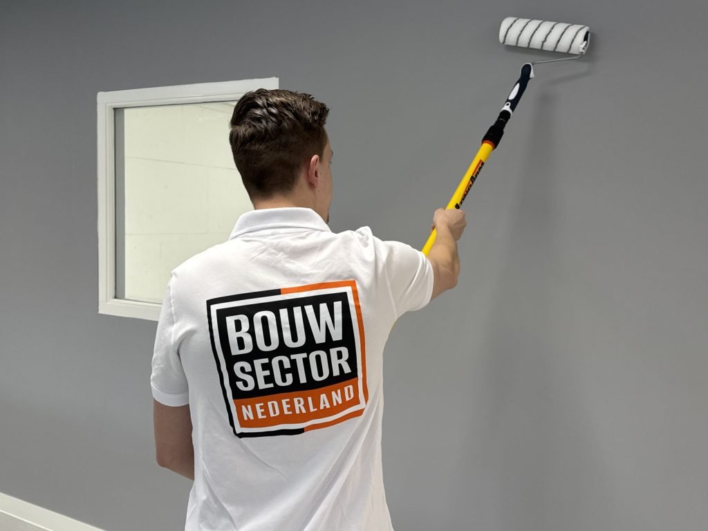 Schilder met het logo van Bouwsector Nederland op zijn rug rolt een grijze muur naast een raam