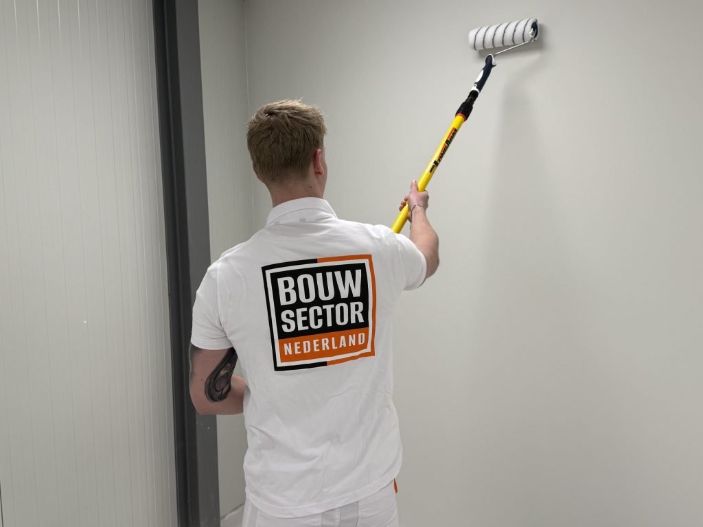 Schilder in wit poloshirt met het logo van Bouwsector Nederland rolt een lichte wand met een verlengsteel