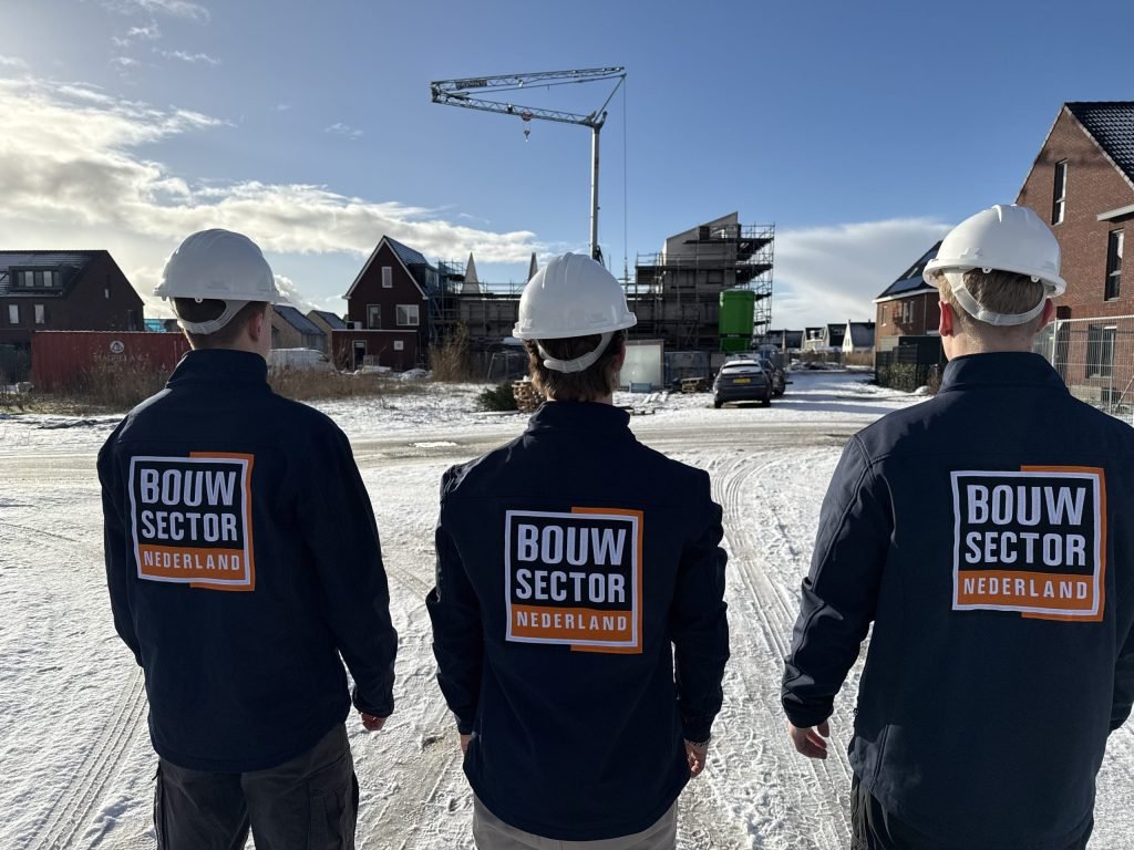 Drie vakmensen van Bouwsector Nederland met witte helm kijken naar rijen nieuwe huizen en een bouwkraan
