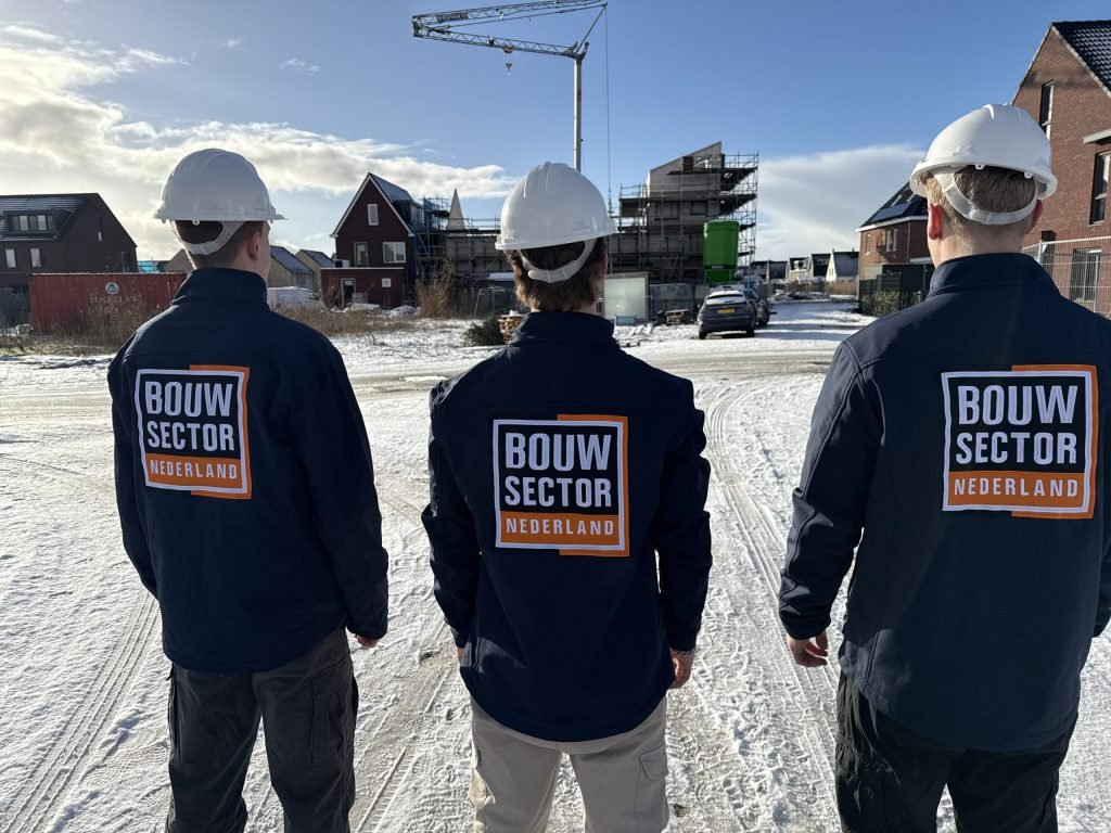 Drie medewerkers van Bouwsector Nederland in donkere jas met helm op een besneeuwde straat bij woningen in aanbouw