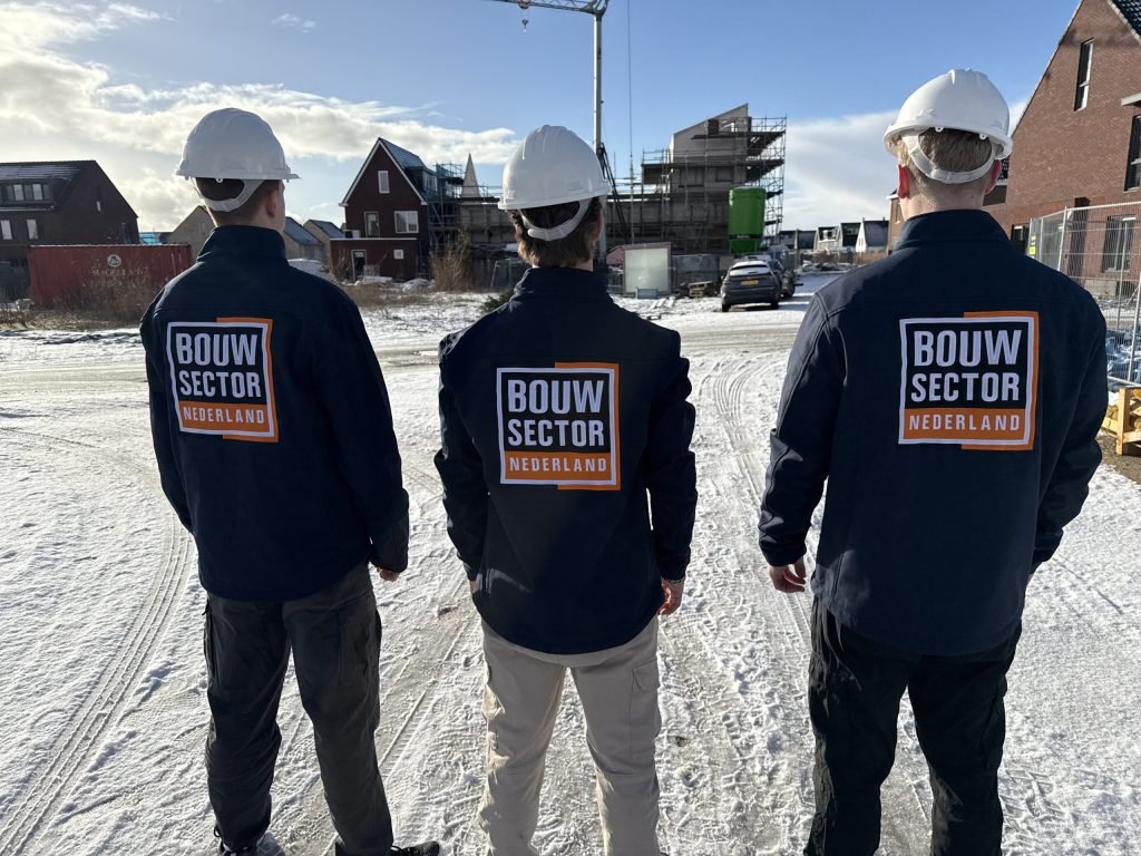 Drie vakmensen van Bouwsector Nederland met witte helm op een besneeuwde bouwplaats met nieuwe huizen in de steigers